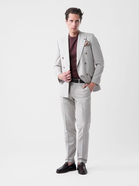 Un uomo in abito grigio chiaro e camicia bordeaux posa con disinvoltura davanti a uno sfondo bianco, con una mano sulla giacca e l'altra in tasca.
