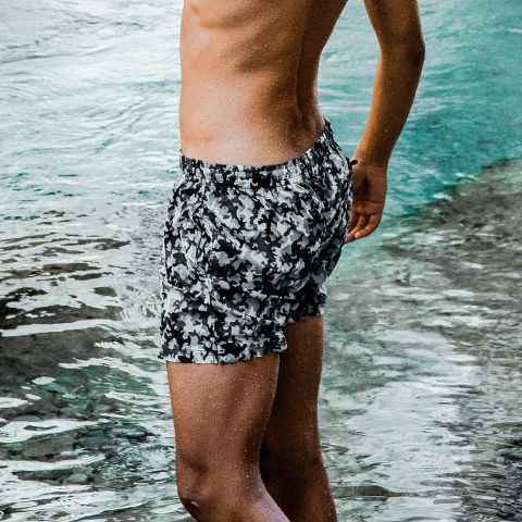 Una persona in piedi in acqua bassa, che indossa un costume da bagno mimetico bianco e nero, con la parte superiore del corpo non visibile nell'immagine.