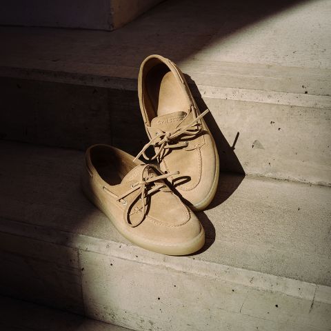 Un paio di scarpe da barca beige in camoscio con lacci, appoggiate su gradini di cemento baciati dal sole.