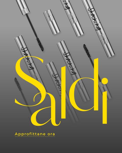 Tubetti e scovolini di mascara argentati disposti in diagonale su sfondo grigio con una grande scritta gialla "Saldi" e una scritta più piccola "Approfittane ora".