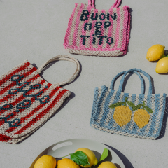 Tre borse in tessuto colorato, due con testo in italiano e una con limoni, sono appoggiate su una superficie chiara accanto a un piatto con limoni e basilico.