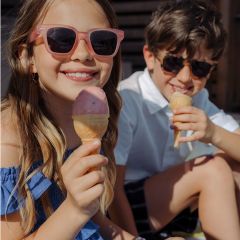 Due bambini sorridenti con occhiali da sole si godono dei coni gelato all'aperto in una giornata di sole.