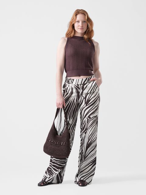 Una donna indossa un top marrone senza maniche, pantaloni larghi con stampa zebrata, sandali neri e una borsa Coach marrone.