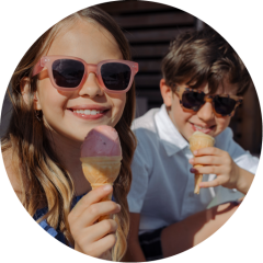 Due bambini sorridenti con occhiali da sole si godono dei coni gelato all'aperto in una giornata di sole.