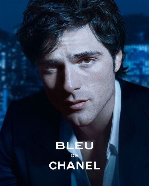 Un uomo in un abito scuro guarda attentamente la telecamera, mentre le luci della città sfumano sullo sfondo; il testo recita "Bleu de Chanel".