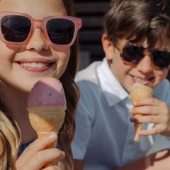 Due bambini sorridenti con occhiali da sole gustano coni gelato all'aperto in una giornata di sole.