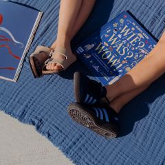 Due persone sono sedute a gambe distese su una coperta blu all'aperto, con sandali e scarpe da ginnastica, accanto a due libri aperti, uno dei quali con copertina blu.