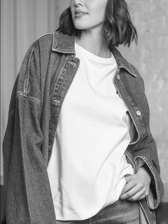 Una donna con una giacca di jeans e una maglietta bianca, che posa con una mano in tasca; l'immagine è in bianco e nero.