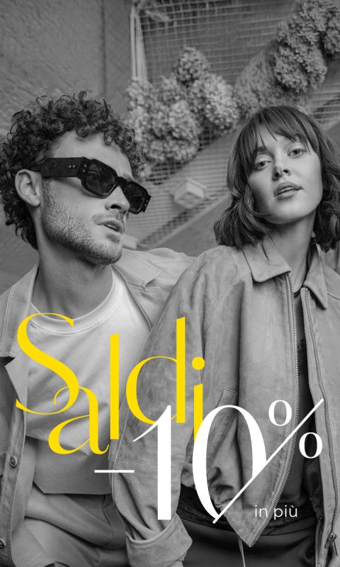 Un uomo e una donna elegantemente vestiti posano in outfit alla moda. Il testo sovrastante in italiano recita „Saldi - 10 % in più“ e indica uno sconto aggiuntivo del 10 %.