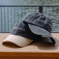 Due cappellini da baseball su una superficie di legno vicino all'acqua; su uno c'è scritto "ASK ME FOR ID" e sull'altro "Formentera Social Club".