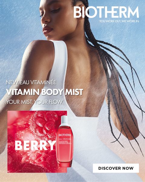 Una donna vestita di bianco sta con la schiena rivolta verso la telecamera nella nebbia. È visibile una bottiglia di „Biotherm Vitamin Body Mist“; il testo pubblicizza la fragranza „Pulsation Berry“.