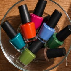 Una ciotola di vetro, riempita con sette boccette di smalto per unghie in vari colori, tra cui blu, rosa, arancione, verde, verde acqua, verde lime e marrone.
