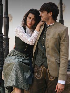 Una donna e un uomo in abiti tradizionali bavaresi sono seduti insieme all'aperto, sorridono e si guardano.