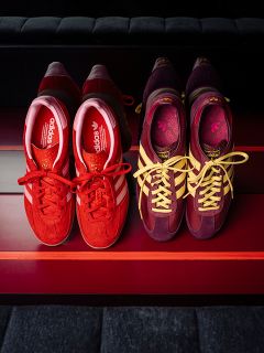 Due paia di sneaker adidas: uno rosso con strisce bianche, l'altro viola con strisce gialle, affiancati su una superficie a strisce rosse.
