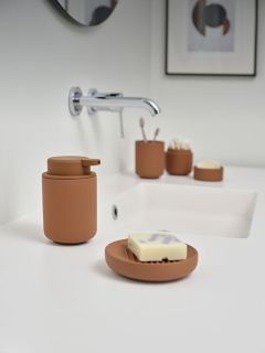Un lavabo moderno con dispenser di sapone marrone, portasapone e accessori su un piano di lavoro bianco, e un rubinetto a parete installato sopra.