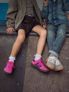 Due bambini sono seduti uno accanto all'altro su una rampa; si vedono solo le loro gambe e le scarpe da ginnastica - uno indossa scarpe rosa, l'altro scarpe da ginnastica grigie e jeans.