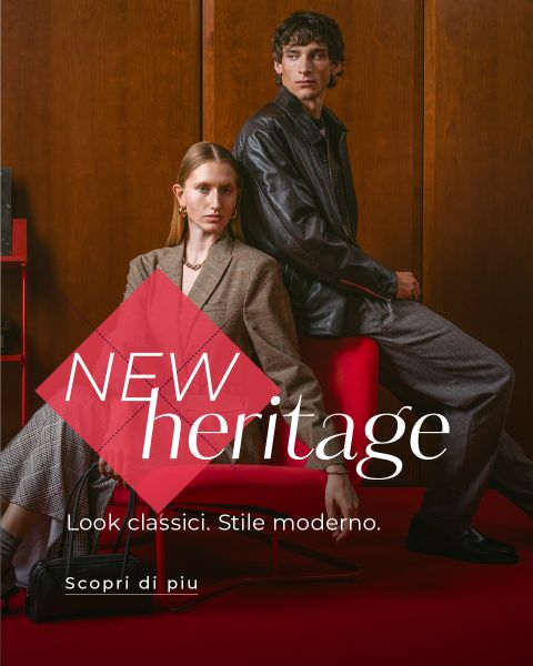 Due modelle in abiti eleganti sono sedute e in piedi accanto a una poltrona rossa, sopra c'è il testo: "NEW heritage. Look classici. Stile moderno. Scopri di più.".