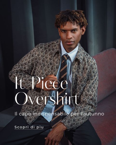 Un uomo in una camicia a fantasia e con una cravatta siede su una sedia davanti a una tenda scura. Un testo in italiano elogia la camicia come capo d'abbigliamento autunnale indispensabile.