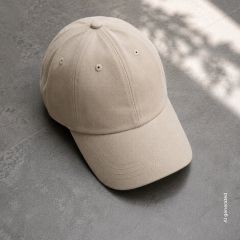 Su un pavimento di piastrelle grigie giace un cappellino da baseball beige, sullo sfondo si vedono luce solare e ombre tenui.