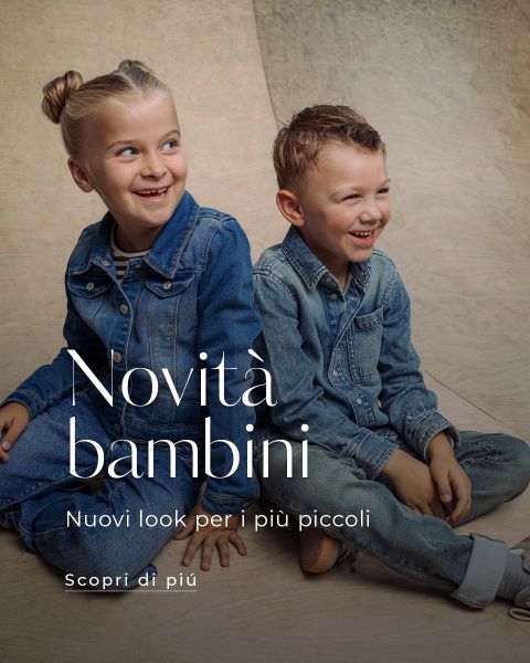 Due bambini piccoli in abiti di jeans sono seduti su una superficie di legno e sorridono. Un testo in italiano promuove nuove tendenze della moda per bambini.