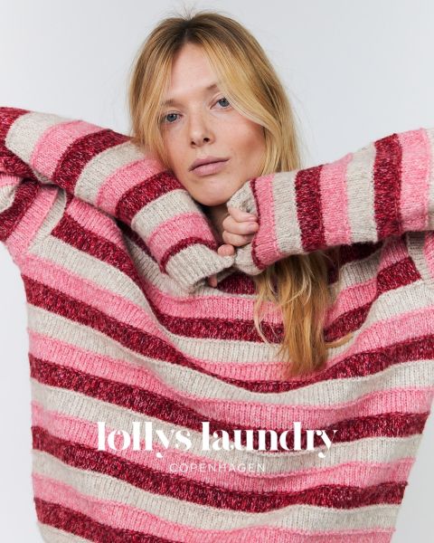 Una donna con un maglione a righe rosa e rosse posa con le braccia alzate davanti a uno sfondo bianco. Sotto c'è la scritta "Lollys Laundry Copenhagen".