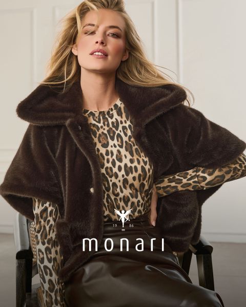 Una donna con un mantello di pelliccia sintetica sopra un top leopardato e una gonna marrone è seduta e in posa; sotto sono visibili "monari" e il logo.