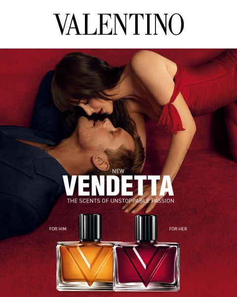 Un uomo e una donna in abiti eleganti si abbracciano su velluto rosso accanto ai flaconi di profumo "Valentino Vendetta", uno etichettato "For Him" e l'altro "For Her".