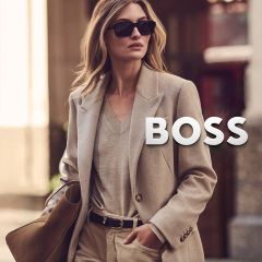 Una donna con un blazer beige e occhiali da sole, che porta una borsa con il logo BOSS.