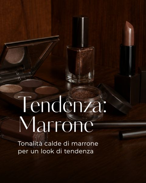 Prodotti make-up marroni - palette ombretti, smalto, rossetto - su una superficie in legno. Un testo italiano promuove le tonalità marroni calde e di tendenza per i look make-up.