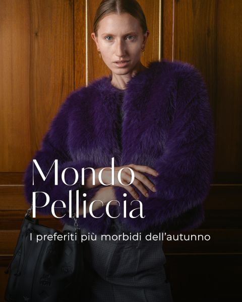 Una donna con una pelliccia viola è in piedi davanti a una parete di legno e tiene in mano una borsa nera. Il testo italiano recita: "Mondo Pelliccia. I preferiti più morbidi dell'autunno.".