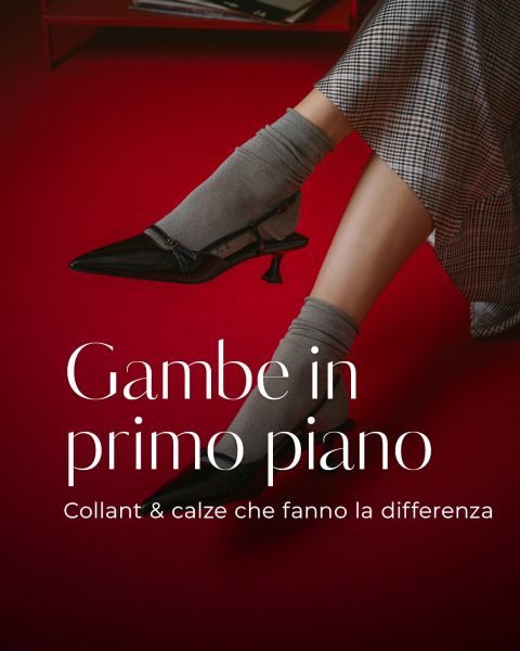 Una persona che indossa calzini grigi e décolleté nere è seduta a gambe incrociate su un pavimento rosso; accanto c'è un testo in italiano sui collant e sui calzini.