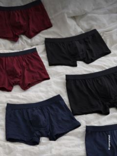 Sei paia di boxer da uomo nei colori nero, bordeaux e blu navy sono stesi su un panno bianco.
