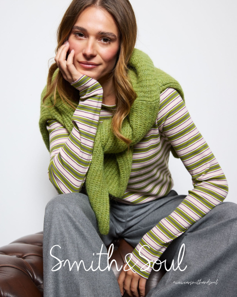 Una donna con una camicia rosa e un cardigan con pantaloni bianchi posa davanti a uno sfondo bianco. Il testo recita "Smith & Soul" in basso.