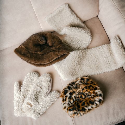 Su un divano beige ci sono quattro accessori invernali in pelliccia, tra cui due cappelli, una sciarpa e dei guanti.
