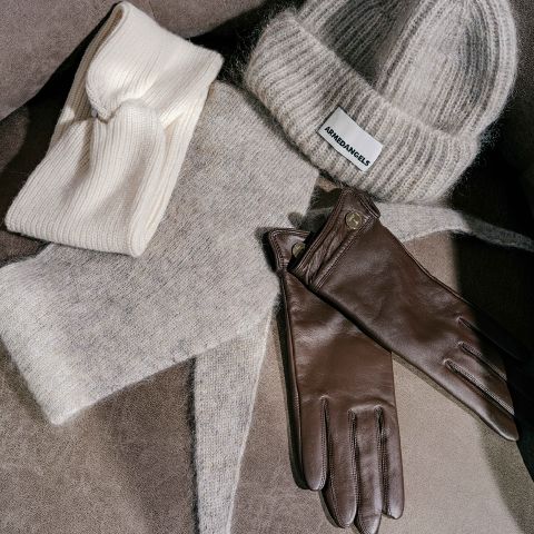 Una fascia in maglia color crema, un berretto in maglia grigio di Armedangels, una sciarpa grigia abbinata e un paio di guanti in pelle marrone.
