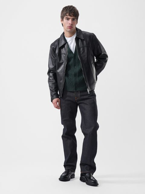 Un uomo che indossa una giacca di pelle nera sopra un cardigan verde, una maglietta bianca, jeans scuri e mocassini neri.
