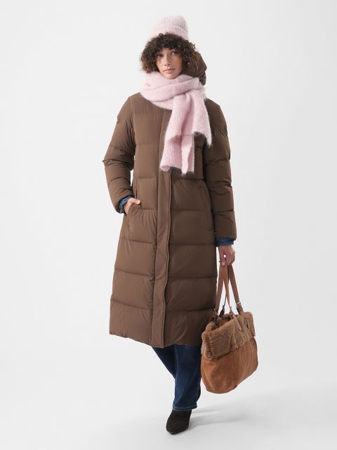 Una persona indossa un lungo piumino marrone, un cappello rosa e una sciarpa rosa, e ha una borsa tote marrone.