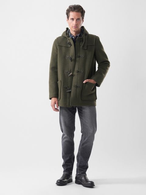 Un uomo indossa un montgomery verde oliva, una camicia button-down, jeans grigio scuro e stivali neri.