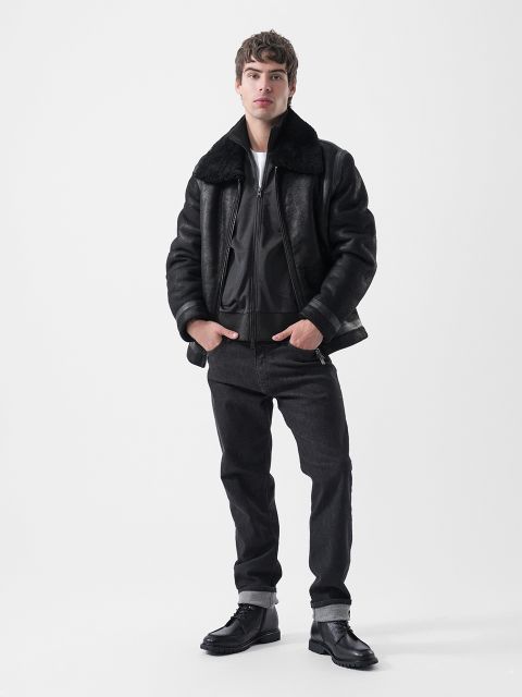 Un uomo che indossa un bomber nero foderato in montone, jeans neri e stivali neri.