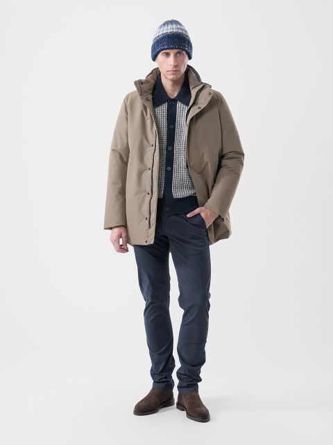 Un uomo che indossa un parka color camoscio sopra una maglia fantasia, abbinato a pantaloni scuri, stivali marroni e un berretto a maglia a righe.